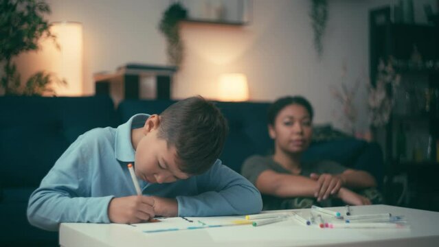 Sad young woman looking son drawing picture, mother worried about child future