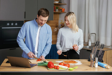 Romantic couple is cooking on kitchen. Handsome man and attractive young woman are having fun together while making salad and pizza. Healthy lifestyle concept.