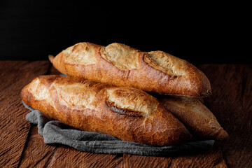 Three french baguettes on a wooden table, dark background close-up