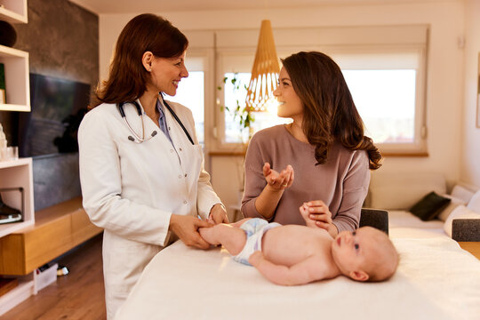 Caring Woman Pediatrician On A Home Visit Talking With The Mother Of The Baby.