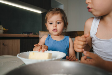 Pretty baby girl and little adorable brother sitting at table in kitchen cooking together pancakes. Family home leisure.