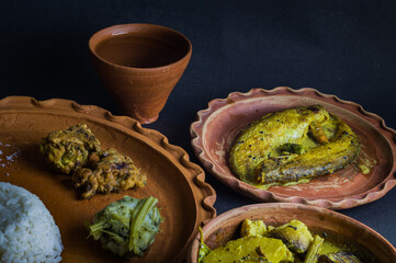 Traditional Bengali indian meal served on clay plate consisting of boiled rice, shukto, fish curry, leafy greens mixed with mashed potato etc, maintaining local bengali culture.