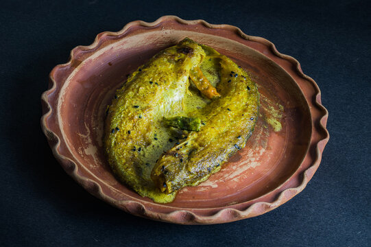 Sorse Pabda fish or Bangladeshi butterfish curry made with mustard in traditional Bengali style served on a clay plate. Photo taken with copy space background