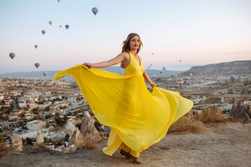 Young woman in yellow dress  during sunrise watching hot air balloons in Cappadocia, Turkey