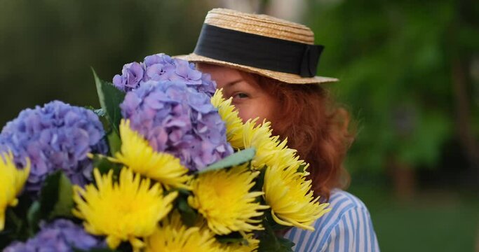 red haired woman laughing and holding a bouquet of blue hydrangea on the background of green garden , spring concept. 4k footage