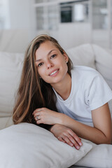 Vertical portrait of pretty caucasian female laying on cozy couch at home looks at camera smiling. Attractive Italian housewife relaxing on weekend. Gorgeous model having rest. Wealthy life.