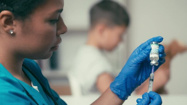 Doctor withdrawing covid vaccine with syringe from ampoule, child immunization