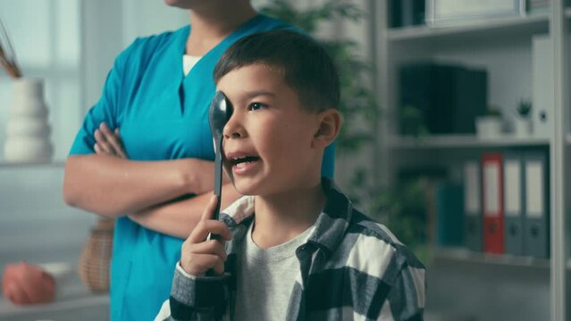 Little boy visiting ophthalmologist, looking at test letters with one eye closed