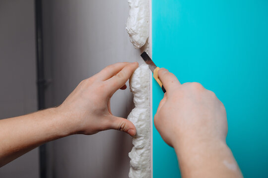 A male's hand cuts the seams of drywall with a stationery knife. The concept of carrying out repair work.