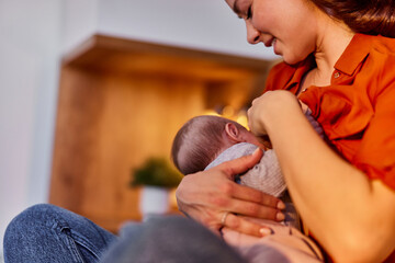 A woman sits with her legs crossed and feeds a baby breast milk at home.