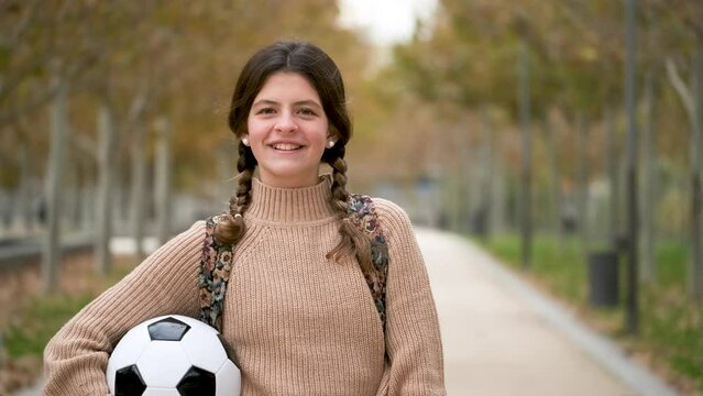 Preteen girl grabbing a soccer ball, smiling and looking at camera outdoors in autumn. Back to school.