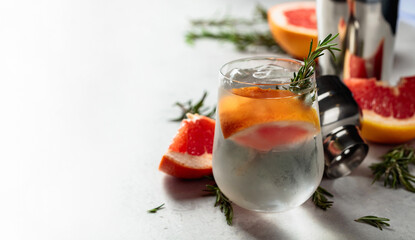 Gin and tonic cocktail with natural ice, grapefruit, and rosemary in a frozen glass.