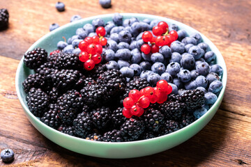 Different mixture of berries - blueberries, blackberries and red currants in a plate on a wooden background. Fruit, berry background.