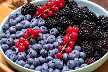 Different mixture of berries - blueberries, blackberries and red currants in a plate on a wooden background. Fruit, berry background.