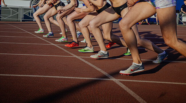 legs female athletes in running spikes Nike and New Balance on starting line of middle distance race, olympic summer sports