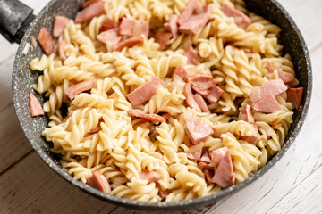 Pasta with bacon, sausage in a pan with a creamy sauce.