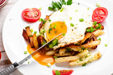 Fried potatoes with egg with liquid flowing yolk, herbs and tomatoes on a white plate.