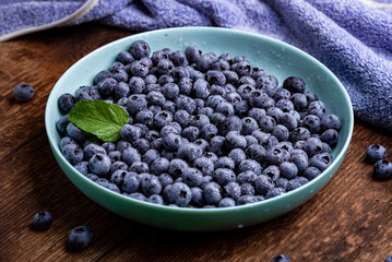 Fototapeta na wymiar Fresh blueberries berries in a plate on a dark wooden background.