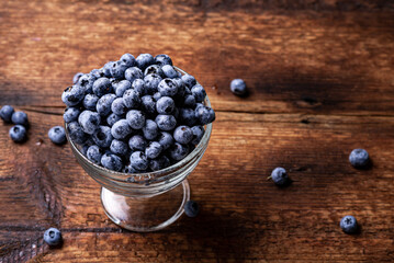 Fresh tasty blueberries in a glass bowl on a dark wooden background.