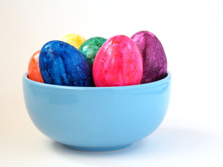 Multicolored eggs in a blue bowl on a white background