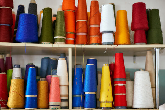 Many bobbins with knitting threads stand in a row on a rack