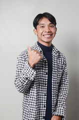 Cute and cheerful Asian man in blue turtleneck and plaid shirt pointing to the side