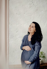 Young pregnant woman with long healthy hair, holds her belly and looking at it with love