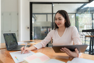 Portrait of Asian businesswoman with laptop writes on a document at her desk in a cafe.