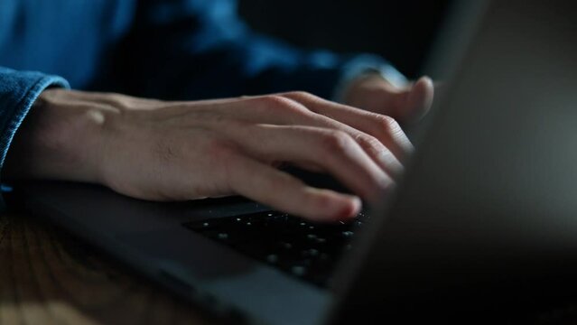 Man typing on his laptop keyboard in a dark studio place at night. Businessman working and doing research on his computer late at night video. Modern pc and office black background