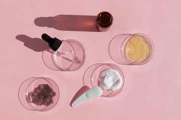 Multicolored texture of cream, scrub and gel with a pipette in a Petri dish on a pink background. The concept of laboratory research of cosmetics. Smears of cosmetic skin care products.