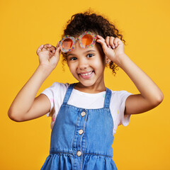 Girl child, studio portrait and sunglasses with smile, happiness and summer style by yellow background. Mixed race model, female kid and fashion frame on face with kids clothes, aesthetic and youth
