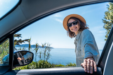 Happy cheerful young woman traveling on the sea by car. Summer vacation and travel concept