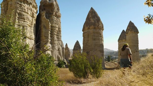 Girl blogger walks in the valley of love. Against the background are sandstone rocks in the form of phalos. In the foreground, bushes and yellow grass sway in the wind