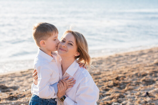 Son of 6 years kisses his young mother of the caucasian ethnicity on the beach in summer. Happy family, single mother brings up her son, divorce, mother's day, mother son relationship, motherhood