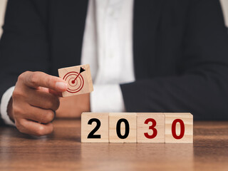 Business planning and strategy in 2030. Hand businessman holding wooden cubes with dartboard icon...
