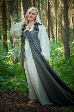 Adult mature woman 40-60 in a green long fairy dress in forest. Photo shoot in style of dryad and queen of nature. Fairy who loves nature in beautiful green summer forest. Concept of caring for nature