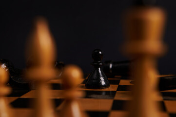 Selective focus on black wooden chess piece, a pawn moving and white pieces on blurred foreground,...