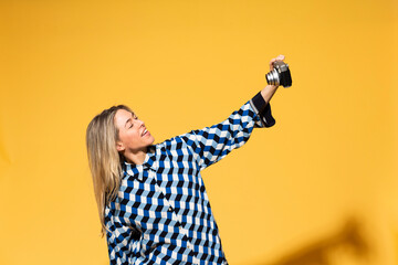 Woman taking selfie through camera against yellow background