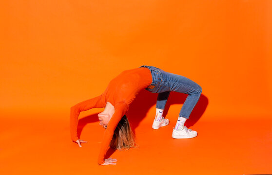 Woman making bridge position against orange background
