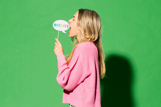 Woman holding speech bubble screaming against green background