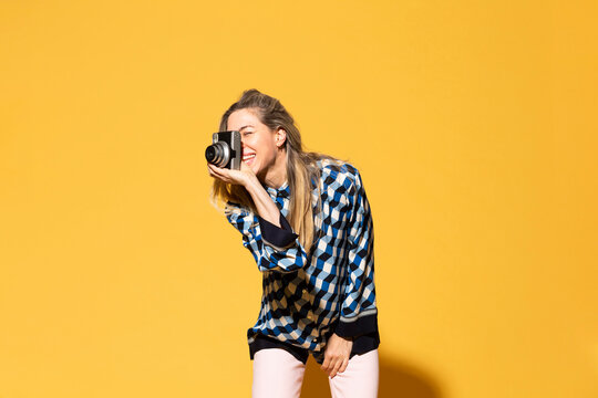Happy woman photographing with camera against yellow background