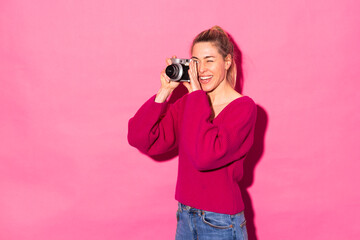 Happy woman taking photo with camera against pink background