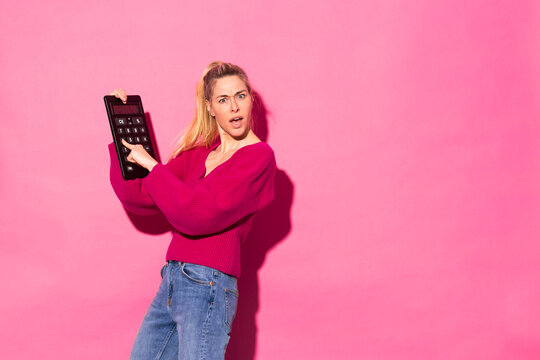 Woman holding big calculator standing against pink background