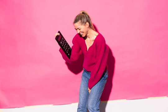 Woman holding calculator standing against pink background
