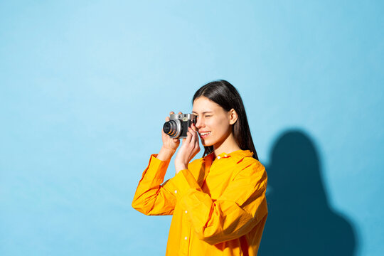 Young woman clicking photo through camera against colored background