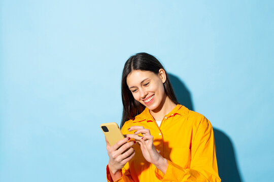 Happy young woman text messaging using smart phone against blue background