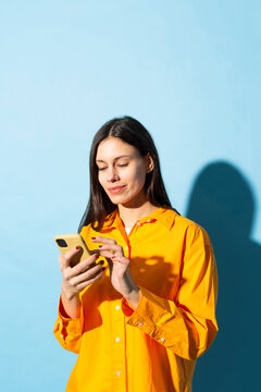Smiling young woman using mobile phone against blue background