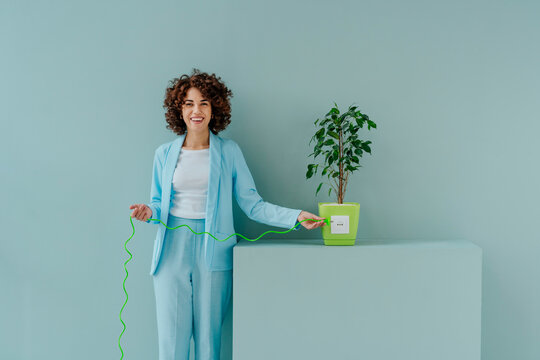 Happy Afro woman inserting plug into socket attached to potted plant