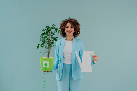 Happy woman holding electric plug inserted in potted plant and watering can