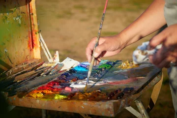 Fotobehang Schilderij Box easel with canvas, oil paint, palette, and tools and Hand of painter with brush on nature outdoors  © keleny